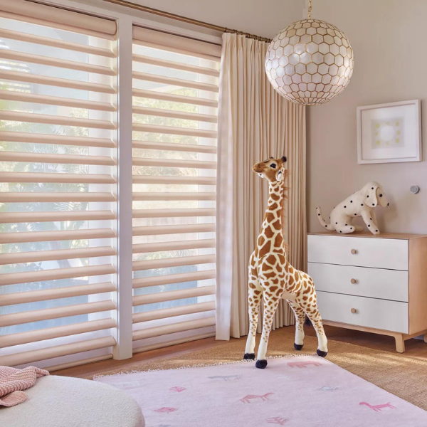 A nursery with Pirouette® shades on the windows and a large toy giraffe. 